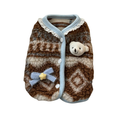 A small pet fleece blanket or vest in a brown and cream geometric pattern, featuring a light blue trim, white lace collar, a small plush bear face on the front, and a matching blue bow with a yellow star accent.